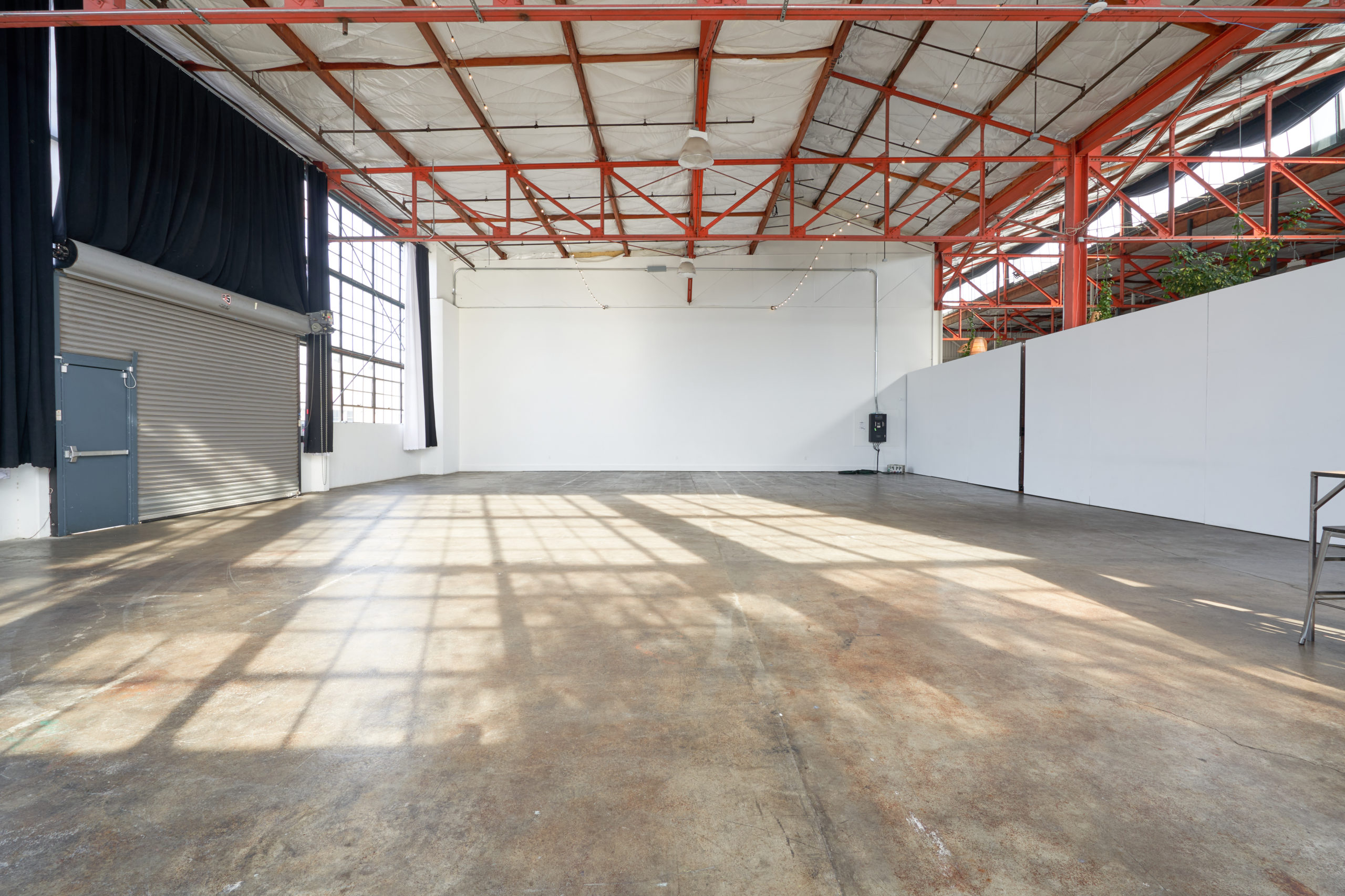 View of the large white wall and the orange industrial beams on the ceiling of expansive Studio 5. There is also a closed loading dock door on the left of the best multiple set studio rental Berkeley has to offer.