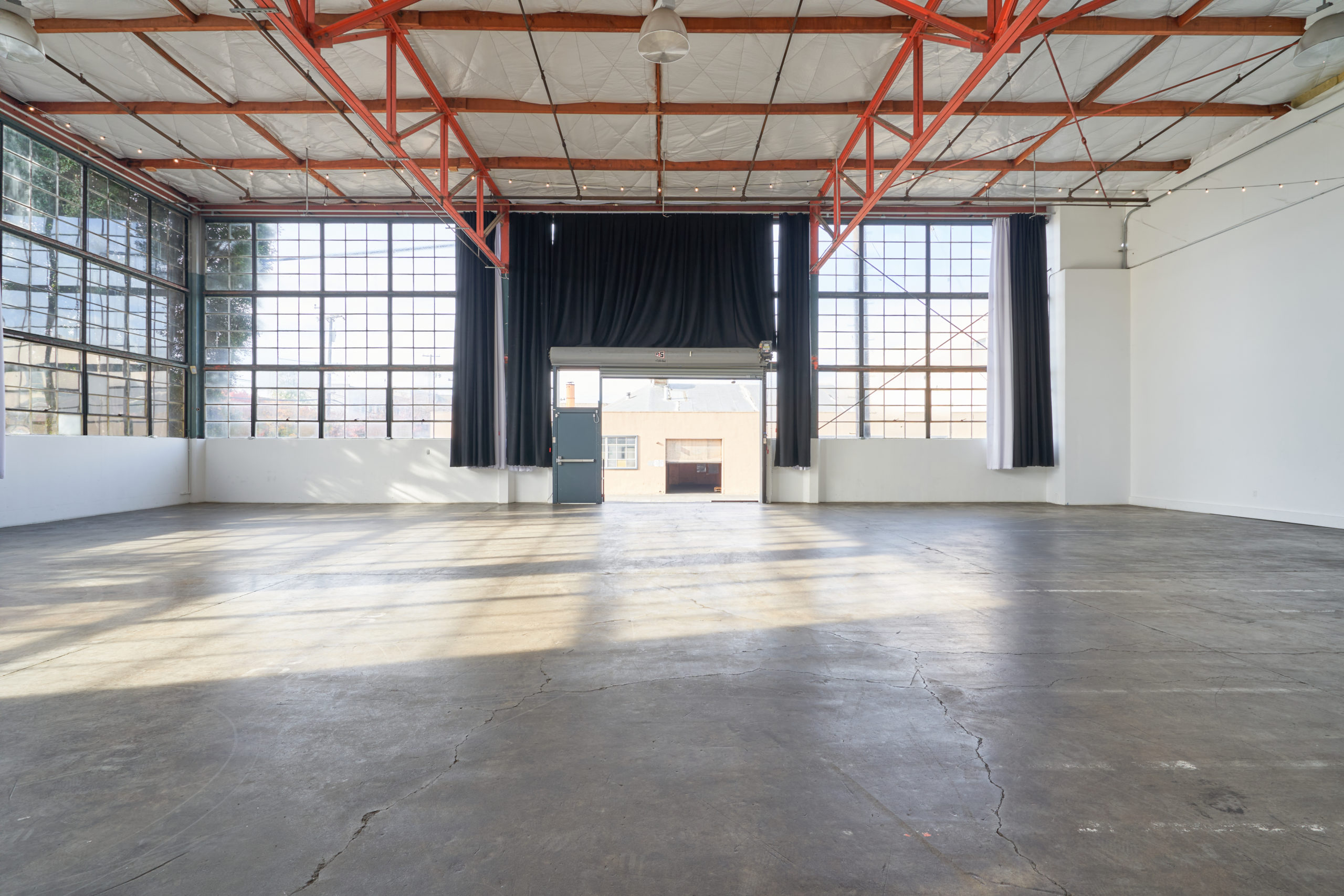View of the private loading dock that leads into Studio 5. The loading dock is surrounded by walls of windows with blackout curtains and there are orange beams on the ceiling inside a multiple set studio rental Berkeley creatives love.