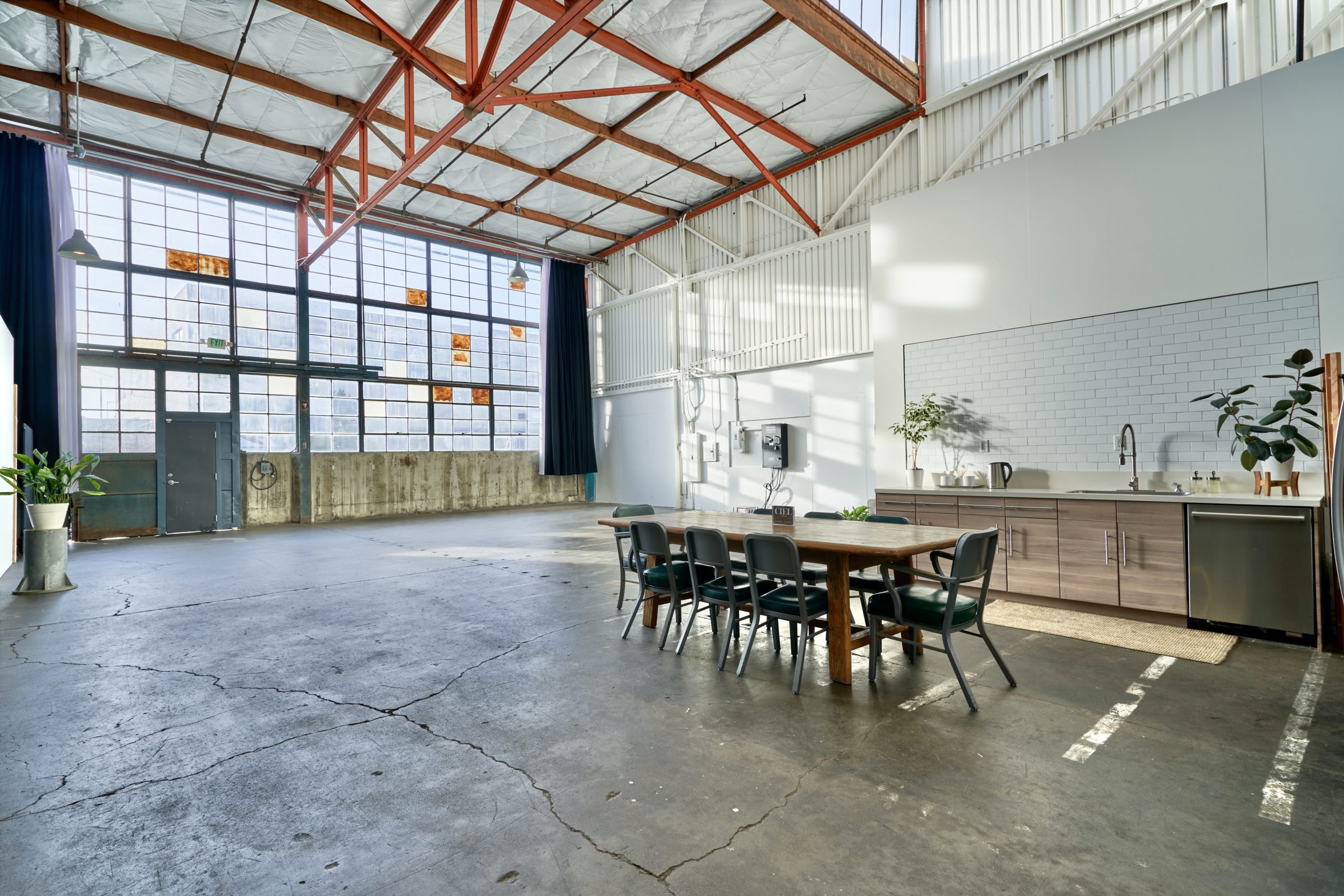 This 2,000 square feet space has lots of light let in from a giant window. It also has a private kitchenette, a ceiling with orange beams, and a large table with seating inside this great creative studio space for rent.