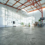 This view of Studio 8 shows how wide open this creative studio space for rent is. Highlights include a ceiling with orange beams, a kitchen, a TV, a fridge, and a large doorway.