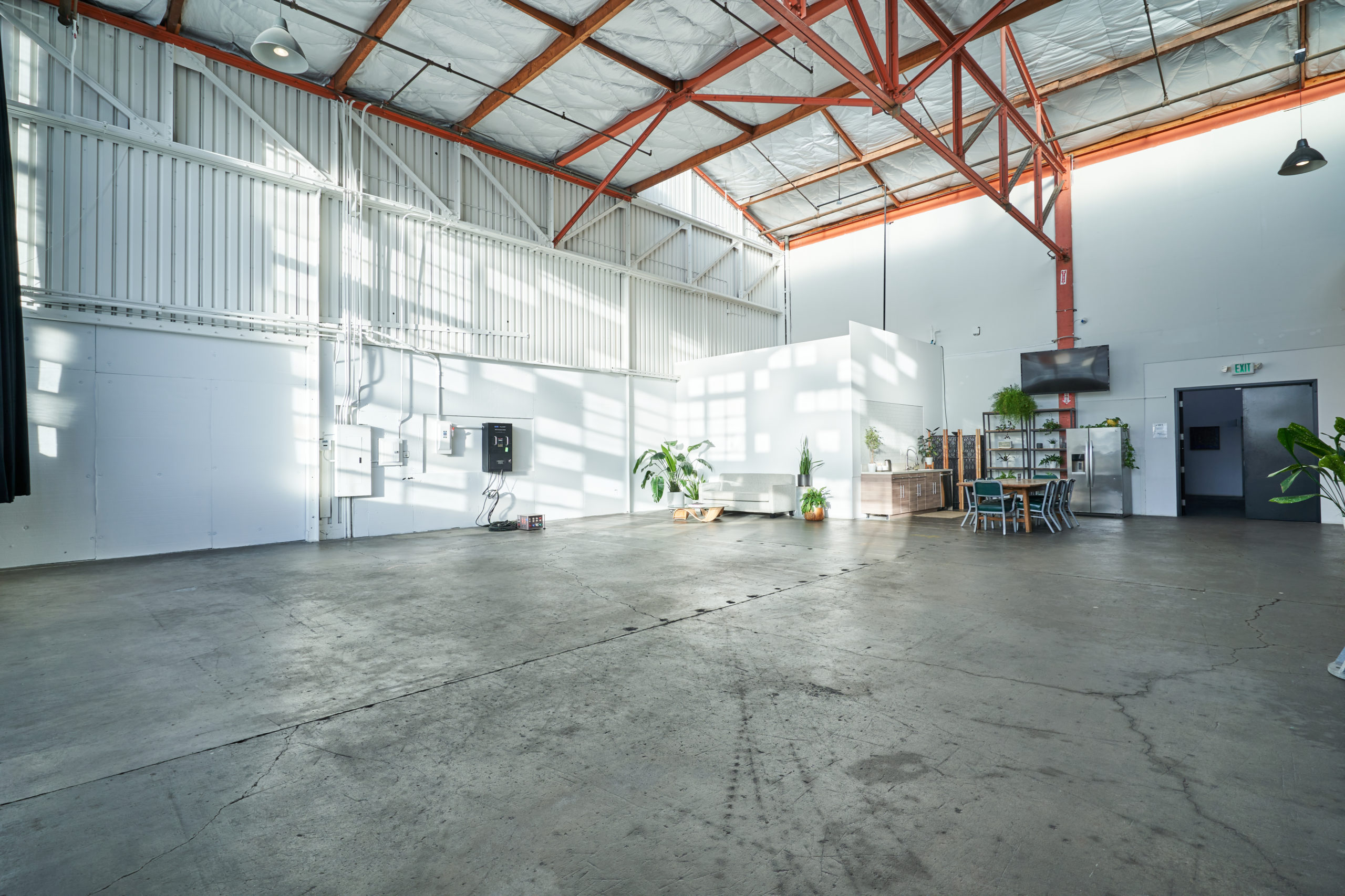 This view of Studio 8 shows how wide open this creative studio space for rent is. Highlights include a ceiling with orange beams, a kitchen, a TV, a fridge, and a large doorway.