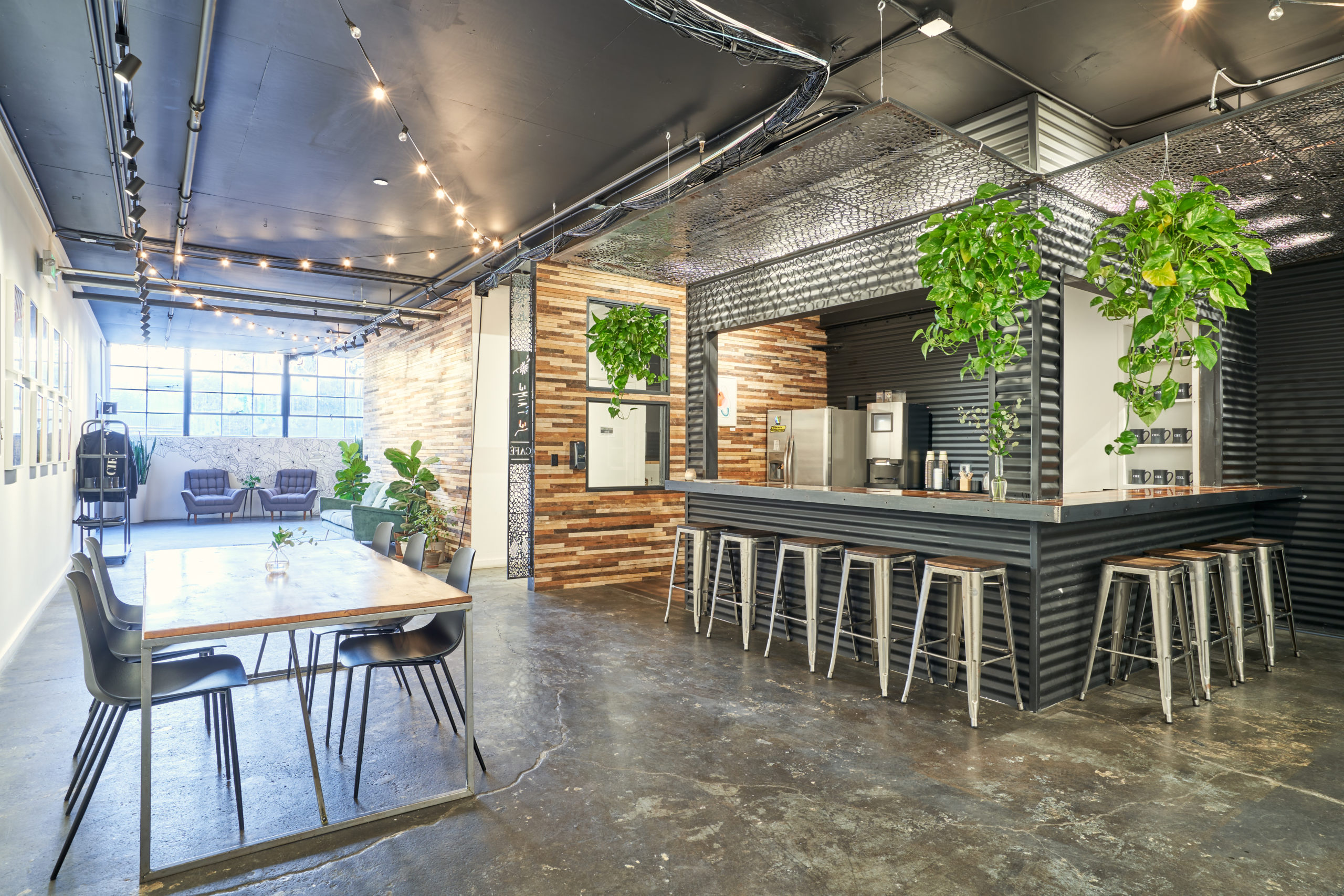 View into the cafe which features a small table, a spacious kitchen with seating at the bar, two chairs, and a small sofa. Green plants along hang around the bar area and add botanical beauty to the best shared offices Berkeley has.