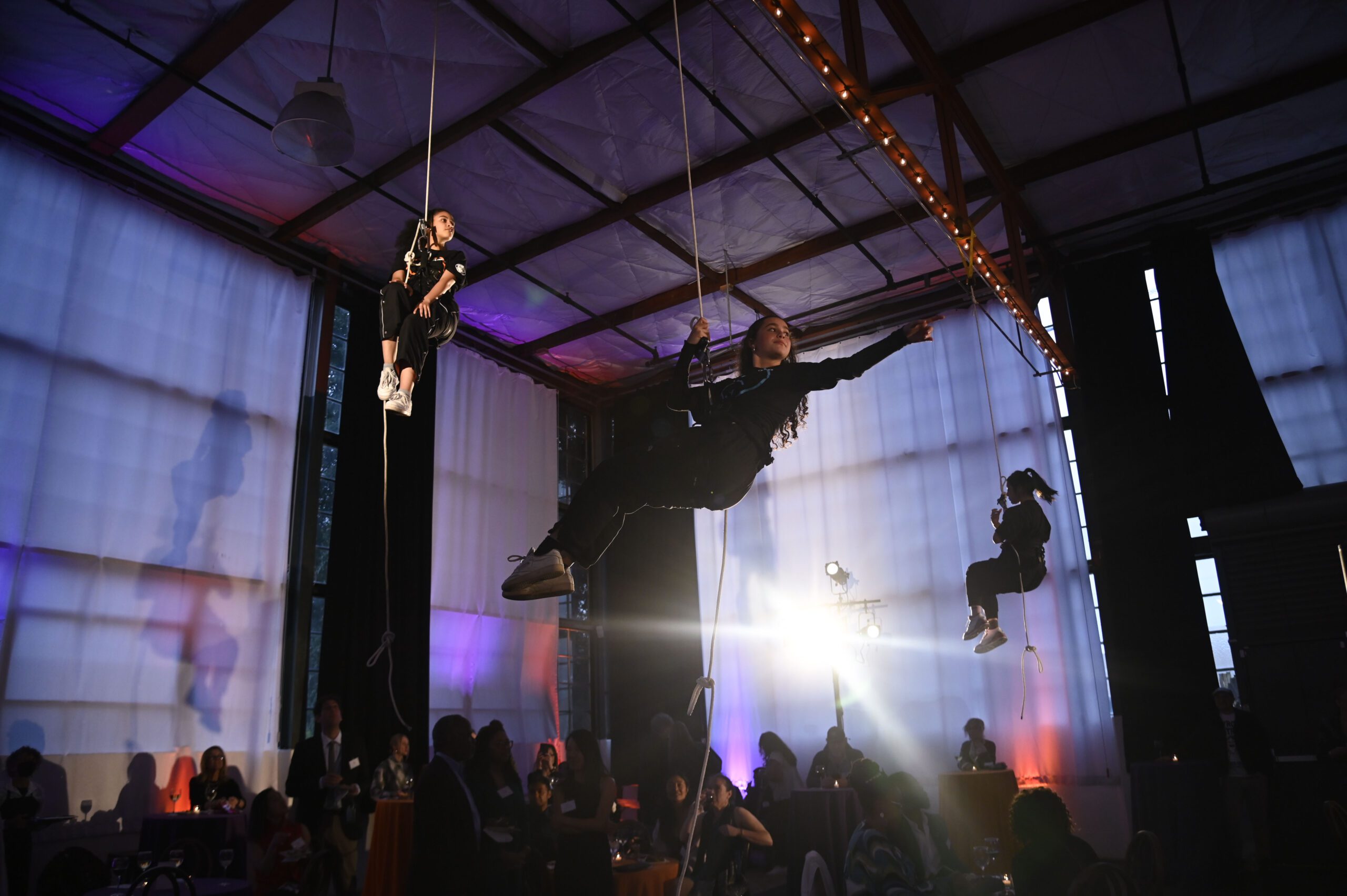 A creative space in Berkeley hosting a live acrobatic event where three people are suspended from the cieling.